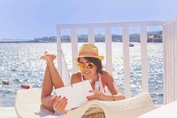 Portrait of Beautiful Young Woman Laying on a Sunbed and  Using Tablet  on a sea Background.Summer Holiday