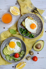 Breakfast for two. Appetizing scrambled eggs in plates, tomatoes, avocado and toast on a yellow serving napkin on a light wooden background. Vertical