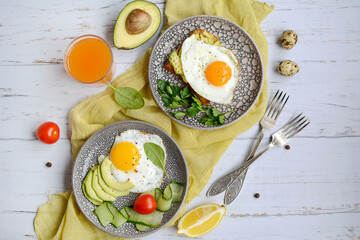 Healthy and tasty breakfast concept. Two plates with eggs and toast with avocado on a yellow napkin and two forks on a wooden background, top view