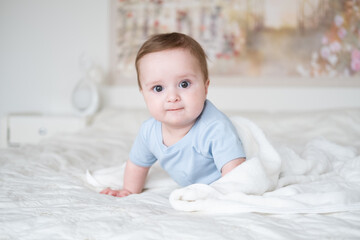 cute baby boy 6 months old in blu bodysuit smiling and lying on bed with white plaid at home.
