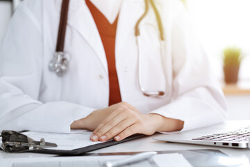 Unknown woman-doctor sitting at the table at working place, close-up of hands. Medicine concept