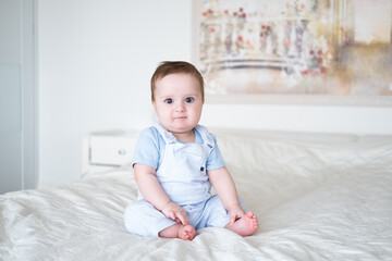 Fototapeta premium baby boy 6 months old in blu clothes smiling and sitting on white bed at home.