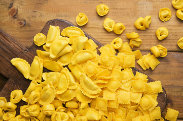 Tartollini with cheese or meat for cooking in broth, different shapes. Traditional dish for celebrations in italy, Emilia Romagna region. Fresh homemade pasta with filling on a wooden table. Above  - obrazy, fototapety, plakaty