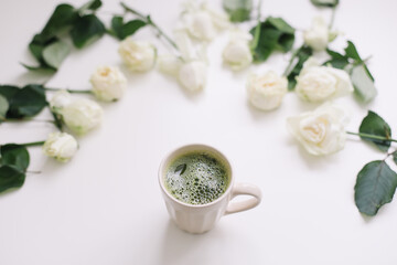 A cup of matcha tea and floral pattern with white roses on white background. Flatlay, top view, copy space