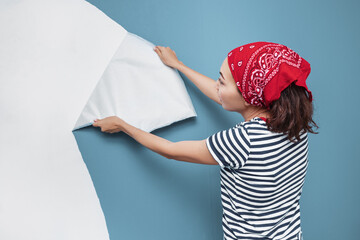 Happy woman housewife peels off an vinyl wallpaper with her hands. The concept of a defect or unsuitable papers when repairing an apartment