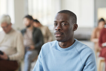Fototapeta premium Portrait of serious African-American man looking at camera while sitting in audience with diverse group of people in background, copy space
