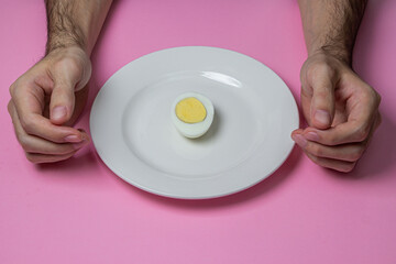 A boiled egg cut in half on a plate. Hands at breakfast. Healthy breakfast. Boiled egg on a pink background.