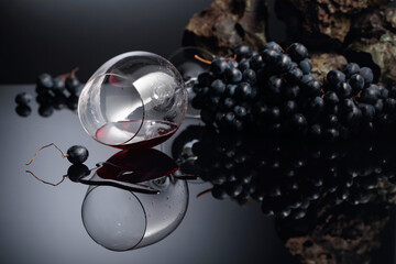 Blue grapes and wine glass with red wine on a black reflective background.