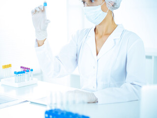 Professional female scientist in protective eyeglasses researching tube with reagents in laboratory...