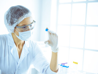 Professional female scientist in protective eyeglasses researching tube with reagents in laboratory...
