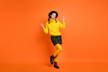Fototapeta na wymiar Full size photo of optimistic funny girl dance hands fists wear yellow sweater cap skirt shoes isolated on orange background
