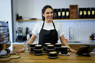 Cheerful brunette woman barista enjoying job in coffee shop having a lot of orders with hot...