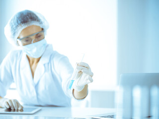 Professional female scientist in protective eyeglasses researching tube with reagents in laboratory...