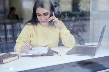 Cheerful caucasian business woman discussing finance report while talking on mobile phone in coffee...