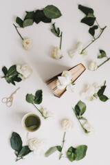 floral composition with a book with white roses and a cup of green matcha tea on a white background, top view,