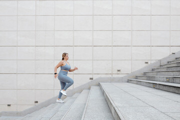 Fototapeta na wymiar Determined fit plus size young woman running up the stairs outdoors, training in city and reaching the goal concept