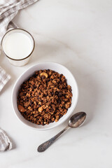 Homemade chocolate granola in a white plate with milk on a light background with copy space. Healthy breakfast