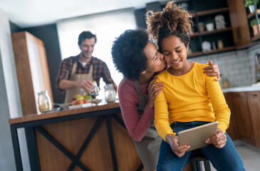 Happy black mother giving a loving kiss to daughter in kitchen