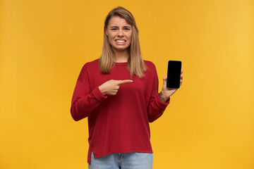 Girl looks looks with disgust, frowns, mouth opened, keeps mobile phone in her hand, black screen...