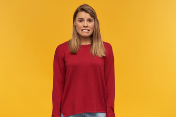 Girl looks looks with disgust, frowns, mouth opened, keeps mobile phone in her hand, black screen turned to the camera, points on it with index finger, isolated on a yellow studio background