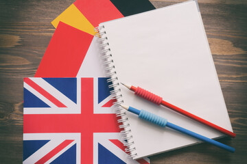 Three national flags, German, English, French, and notebook with blank sheets and two pencils on...