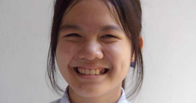 A white young Asian teenage high school student girl is smiling and has crooked teeth on the side.