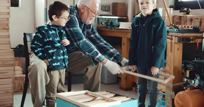 Grandfather and grandchildren play in the garage while making beehives together. Happy family working at home, making wooden frames. Retired hobby