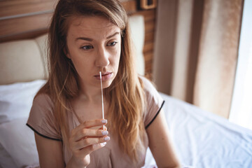 Young woman holds a swab into her nose and holds a medical tube for the coronavirus / covid19 home test. Coronavirus nasal swab test for infection. COVID-19 swab collection kit.