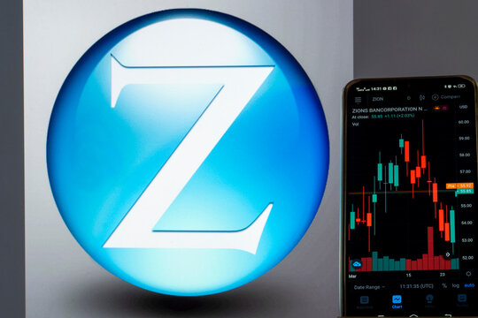 In this photo illustration the stock market information of Zions Bancorporation seen displayed on a smartphone with the Zions Bancorporation logo in the background.