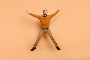 Fototapeta na wymiar Full size photo of optimistic brown hair man jump wear brown sweater pants shoes isolated on beige color background