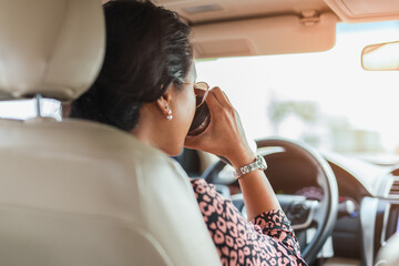 Asian woman drinking hot coffee from vacuum flask while driving a car.