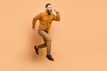 Fototapeta na wymiar Full size profile photo of optimistic brown hair man jump wear brown sweater pants shoes isolated on beige color background