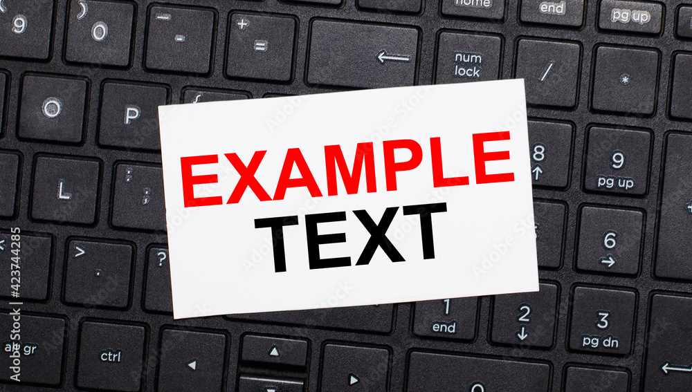 Aufkleber on a black computer keyboard there is a white card with the text example text. view from above