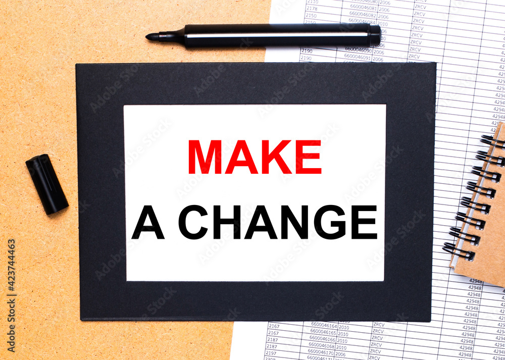 Poster on a wooden table, there is a black open marker, a brown notepad and a sheet of paper in a black fra