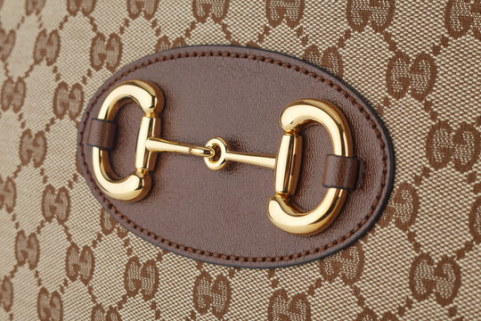 Gold metal Gucci buckle on brown leather serves as a decoration for Gucci textile bags with an embroidered logo arranged in a checkerboard pattern. Belarus, Minsk, 19.12.2020.