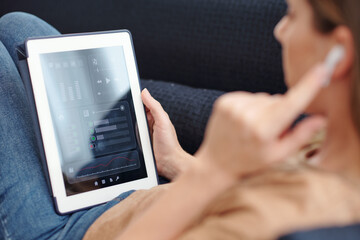 Young woman listening to music in earbuds and setting volume via application on tablet computer