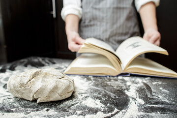 Kneaded dough lies on a table sprinkled with flour, against the background of a baker leafing...