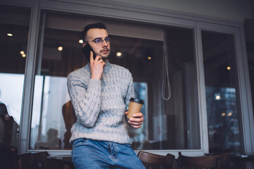 Focused man talking on phone and holding cup of beverage