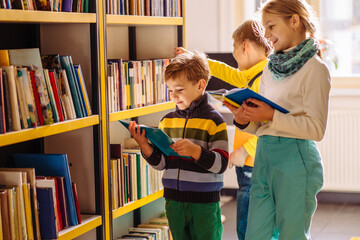 Cute different age pupils, two boys and girl looking for books in library at the elementary school....