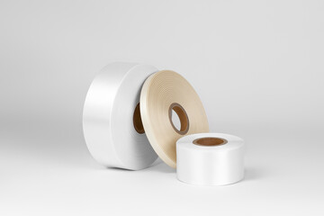 composition of three coils of white, beige satin ribbons of different sizes for labels or branding, isolated on a white, gray background.