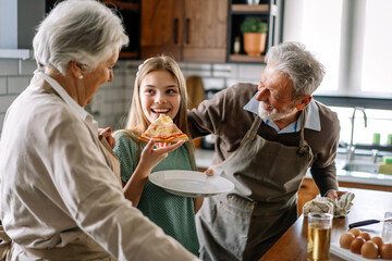 Happy family with grandparent and child in kitchen eating pizza