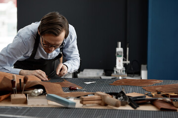 Fototapeta na wymiar Skilled leather manufacture worker cutting some samples