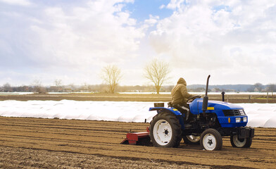 Farmer on a tractor with milling machine loosens, grinds and mixes soil. Loosening the surface,...
