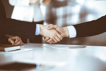 Business people shaking hands at meeting or negotiation, close-up. Group of unknown businessmen, and a woman on the background in a modern office. Teamwork, partnership and handshake concept