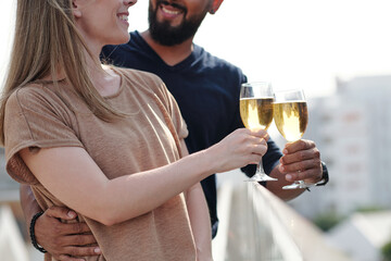 Cropped image of smiling hugging young couple enjoying drinking champagne on rooftop