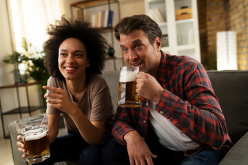 Boyfriend and girlfriend drinking beer at home. Happy couple watching sports game on tv.