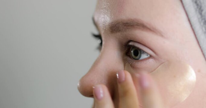 Close-up side view of beautiful caucasian woman using patches under eyes after spa before going out on gray background. Self-care and delicate skin care concept