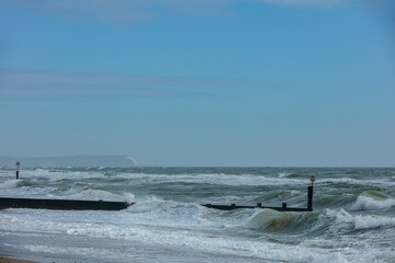 Stormy weather at the beach with crashing waves on a wooden groyne (breakwater) under a majestic blue sky