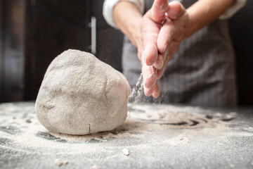 Large lump of kneaded dough on the table with flour, in the background of the baker hands. Bread...