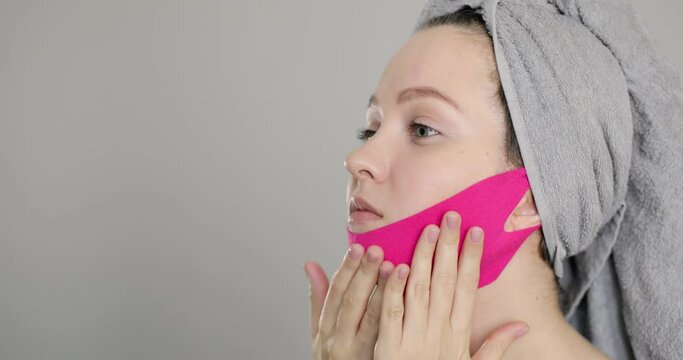 Side view of a young well-groomed european woman wears pink face bandage for chin and oval lift. Concept of cosmetic accessories and procedures